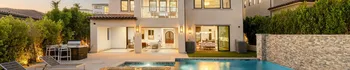 Luxury backyard home exterior with swimming pool, outdoor seating area, modern windows, privacy hedges, and evening lighting
