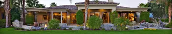 Single-story home exterior with warm evening lights, stone accents, large windows, landscaped front yard, and outdoor living details