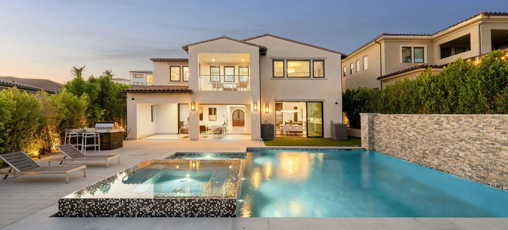 After backyard remodeling project in Los Angeles featuring a luxury pool, raised spa, upgraded patio, outdoor kitchen, modern lighting, stone accent wall, and resort style backyard living space