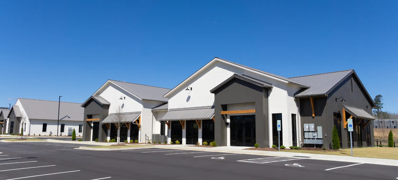 After commercial construction project in Los Angeles featuring completed retail style commercial buildings with modern storefronts, parking lot, accessible spaces, metal roof details, and business property construction