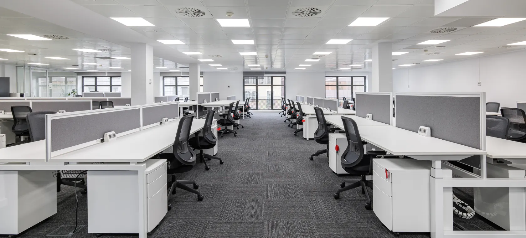 After commercial remodeling project in Los Angeles featuring a modern office workspace with white workstations, updated ceiling lights, gray carpet flooring, open layout, and professional tenant improvement design