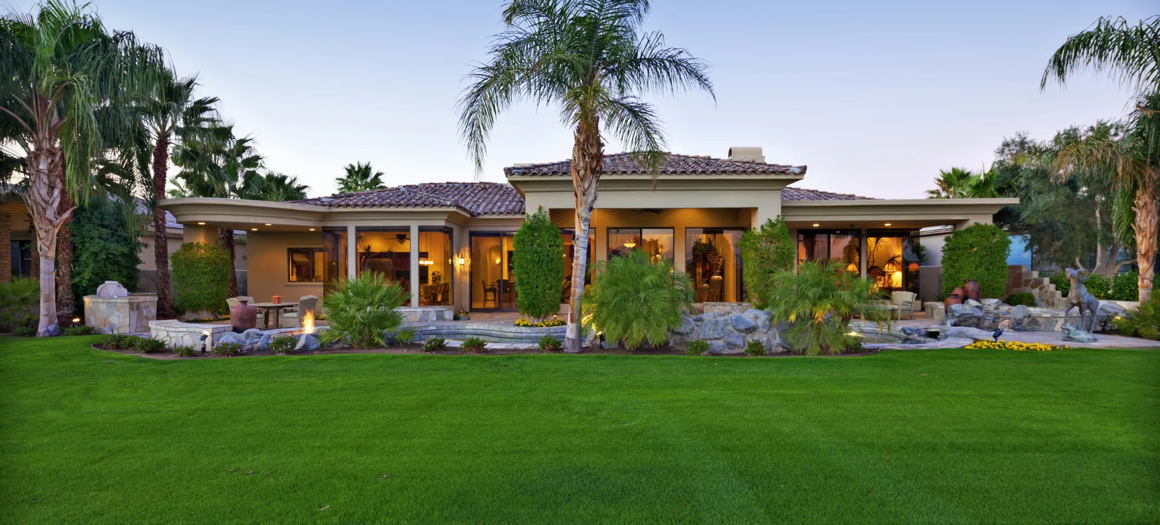 After new construction project in Los Angeles featuring a completed custom home exterior with tile roof, palm trees, landscaped lawn, outdoor lighting, patio areas, and luxury residential design