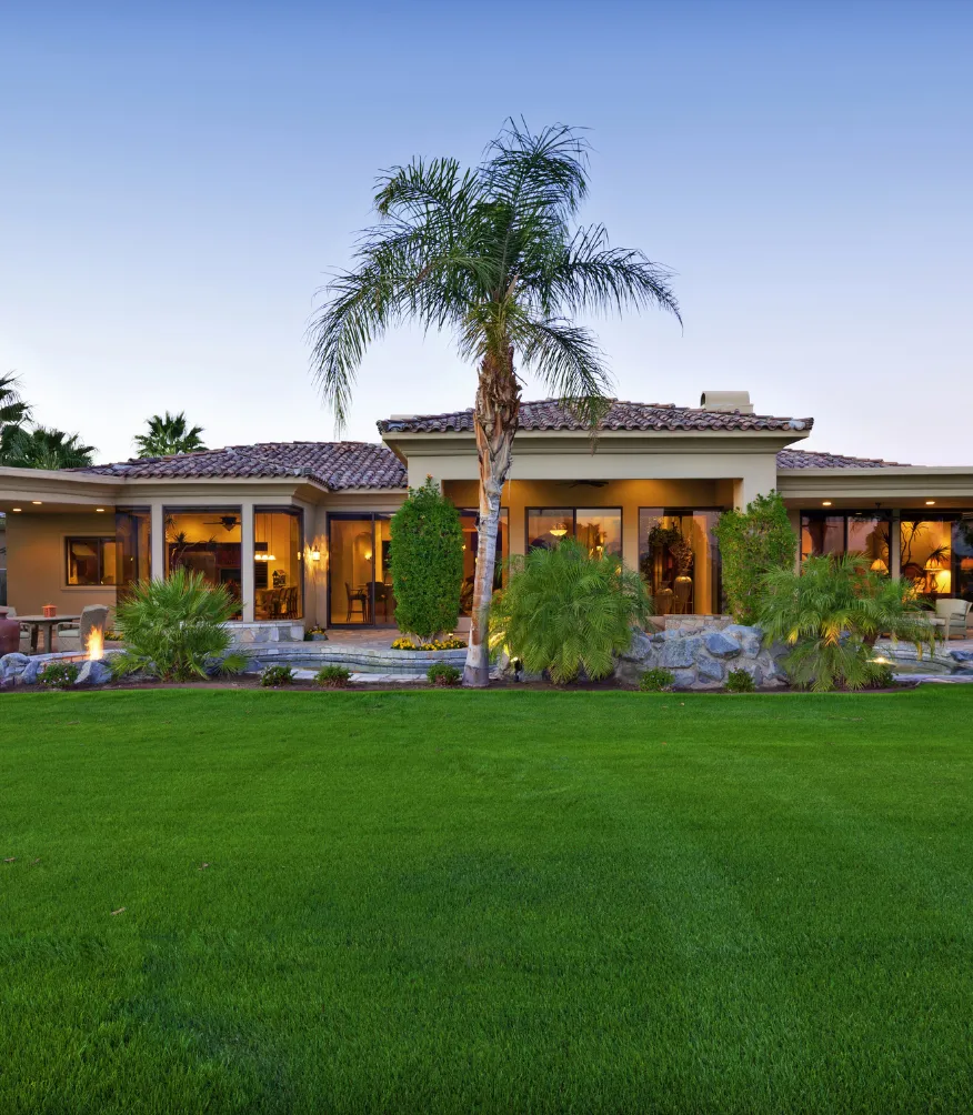 New construction project in Los Angeles showing a completed custom home exterior with stucco finish, tile roof, palm landscaping, large lawn, and luxury residential design