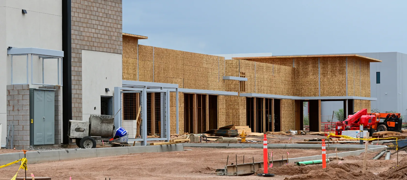 Commercial construction in Los Angeles with large building framing, exterior structural work, job site equipment, safety cones, and active construction progress