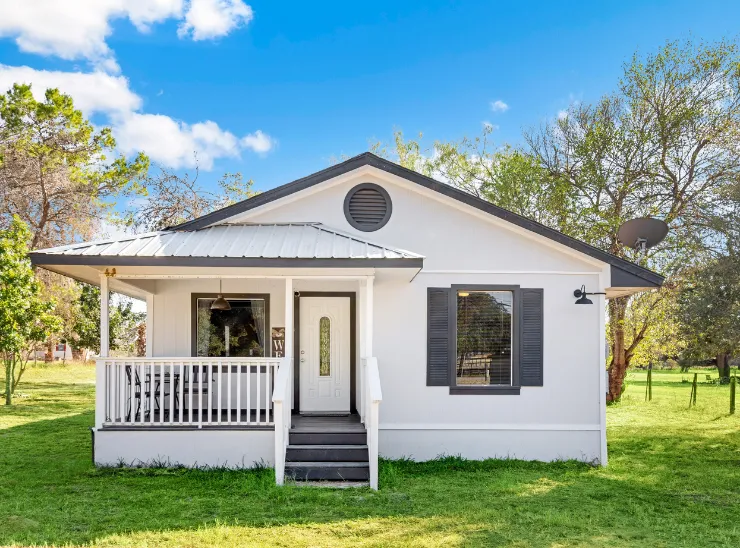 Modern detached ADU built by ADU builders in Los Angeles featuring a white exterior, covered front porch, entry steps, and private yard setting