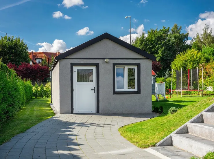 Garage conversion ADU in Los Angeles shown as a finished backyard living unit with a modern gray exterior, front entry door, window, and paved access path