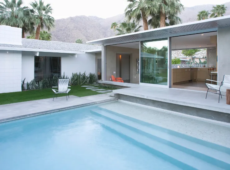 Room additions in Los Angeles featuring a modern home expansion with large glass openings, covered outdoor living area, and poolside design integration